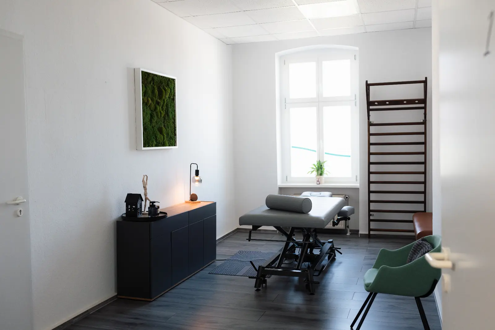 Behandlungsraum 1 der Praxis Tenschert mit Behandlungsliege, Sprossenwand und Mooswandbild