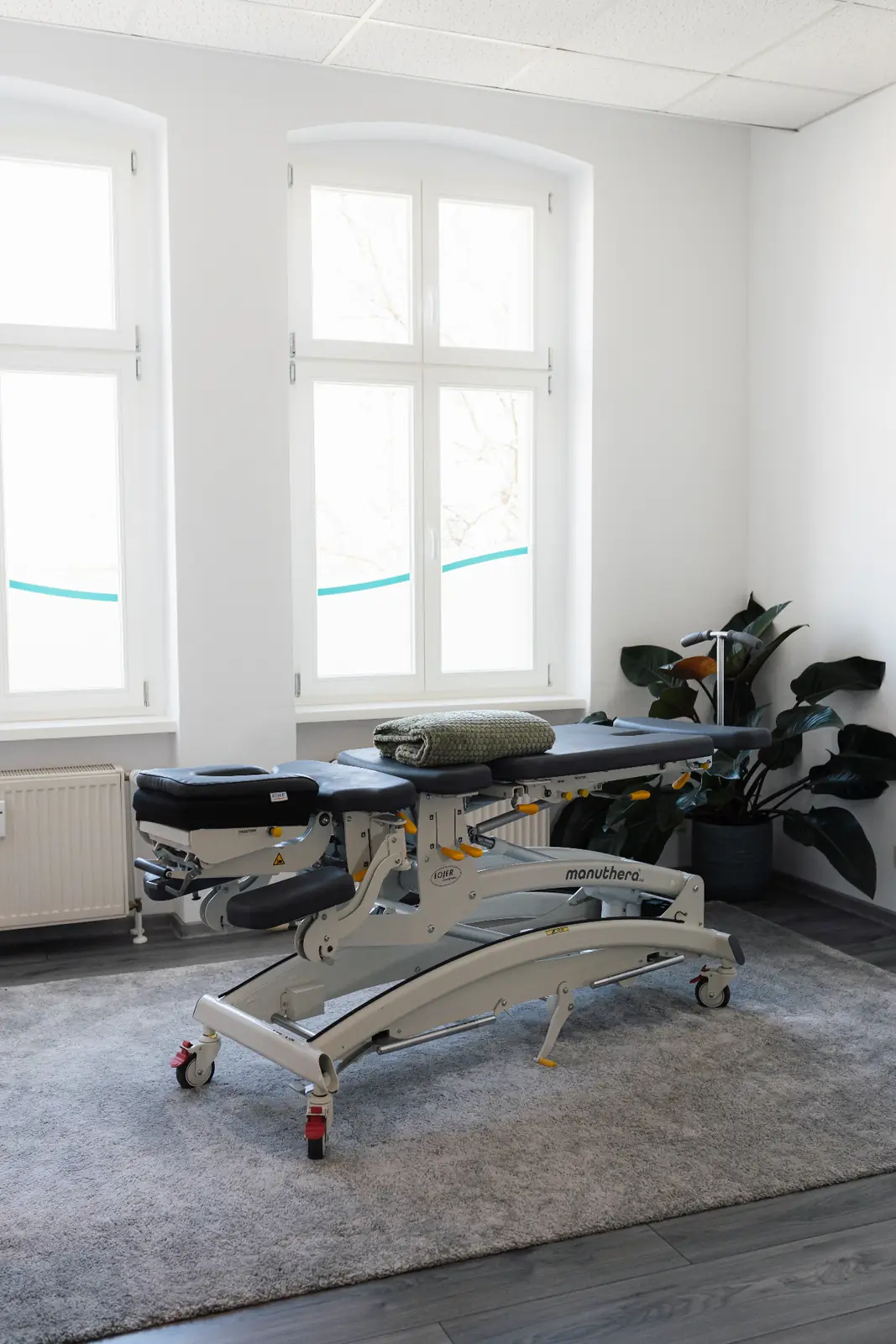 Behandlungsraum 2 der Praxis Tenschert mit Manuthera-Therapieliege vor großen Sprossenfenstern